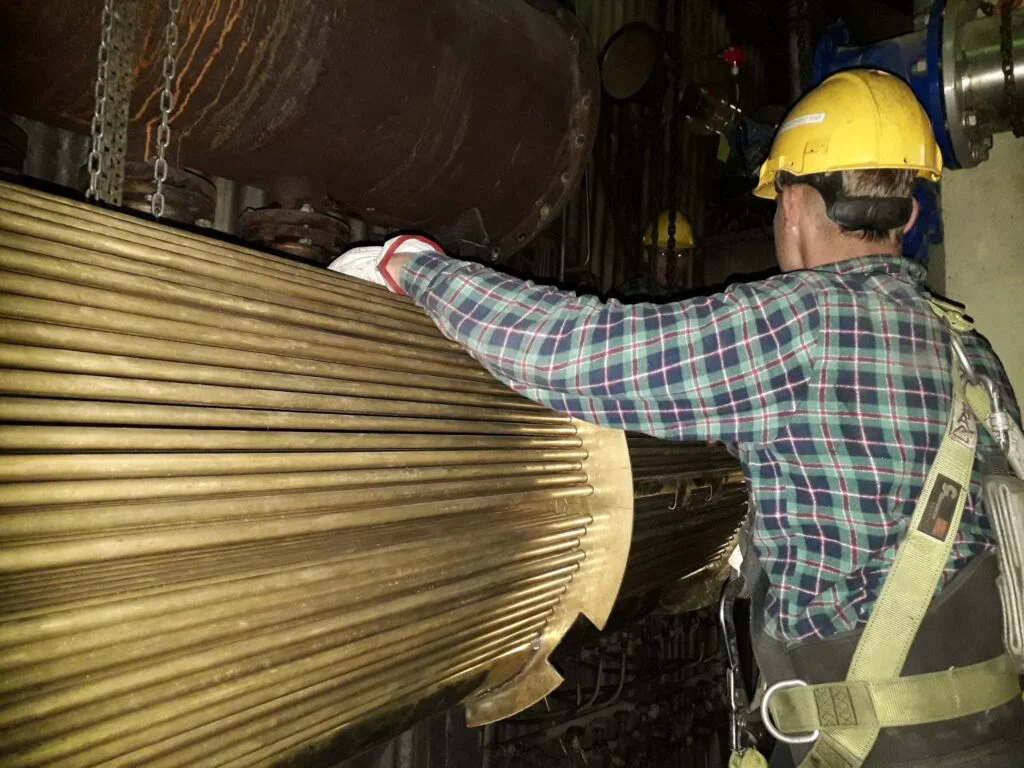 Pracownik w kasku i uprzęży przy metalowej instalacji przemysłowej.