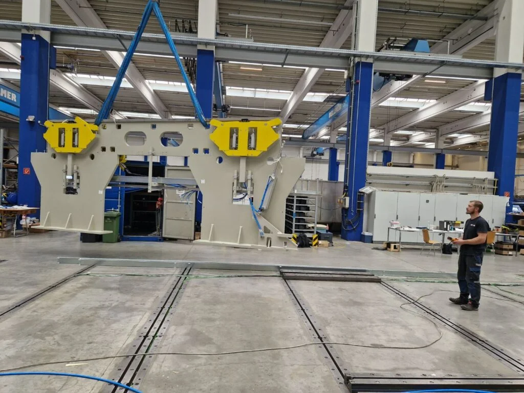 Robot przemysłowy jest podnoszony przez dźwig w hali produkcyjnej.